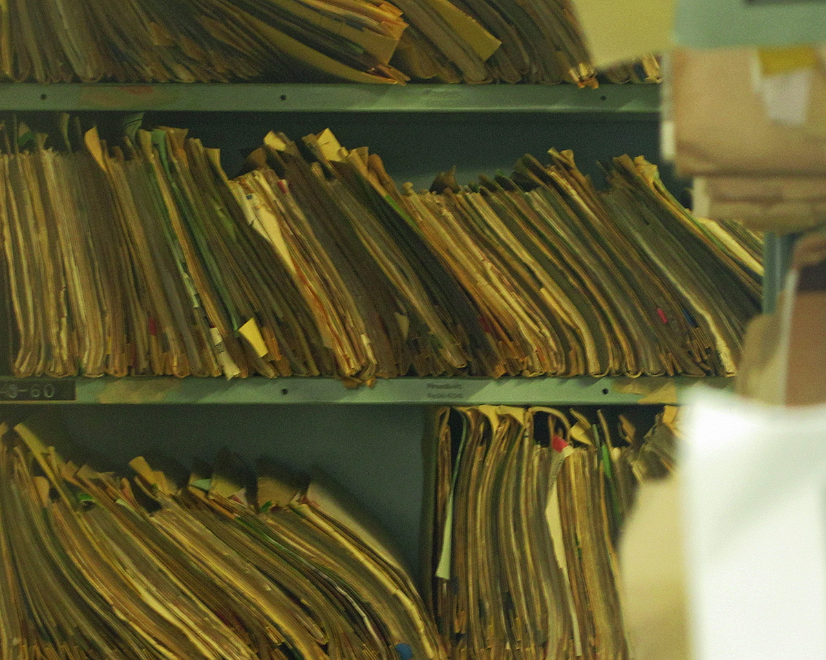 Paper medical record files stored on a shelf.