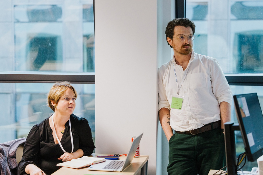picture of Cath Montgomery (sat) and Max Perry (stood) watching presentations during the DARE panel.