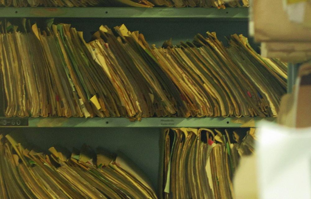 Paper medical record files stored on a shelf.