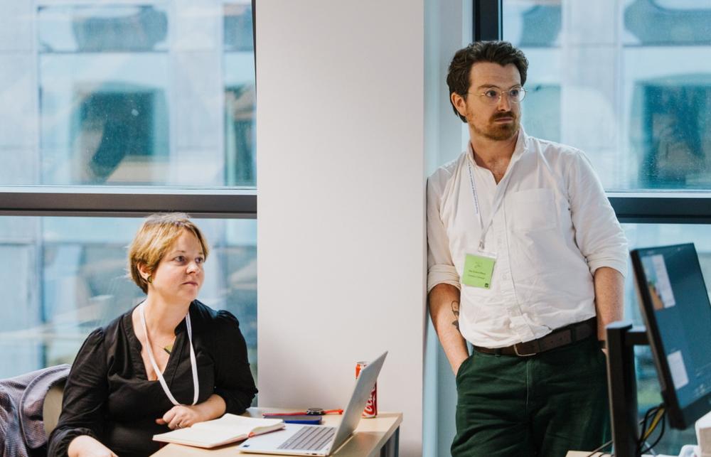 picture of Cath Montgomery (sat) and Max Perry (stood) watching presentations during the DARE panel.